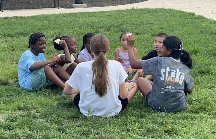 Children and participants playing a circle game on the grass